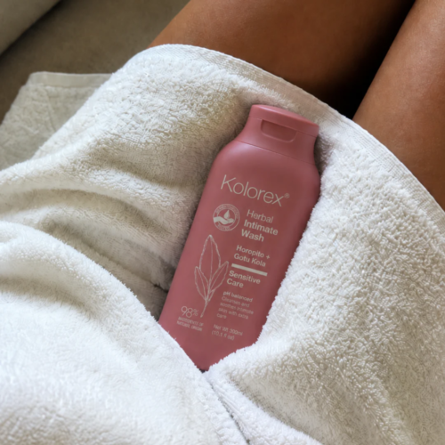 Pink bottle of Kolorex Intimate Wash sitting on a towel between a woman's legs