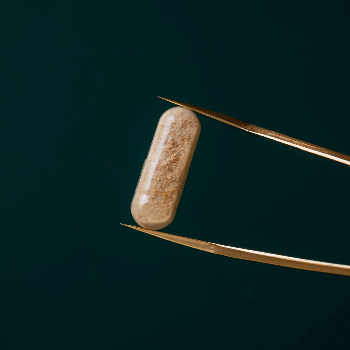 A single V-Spot probiotic pessary held in tweezers against a dark green background